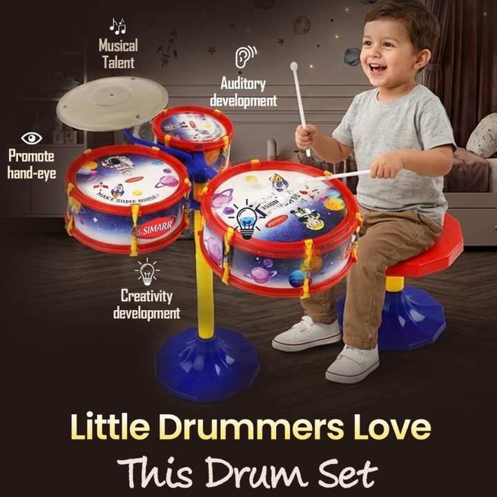 A young child sitting on a small drum stool and playing a colorful toy drum set in a bedroom setting. The drum set has three drums with blue and red bodies, yellow stands, and cartoon graphics.