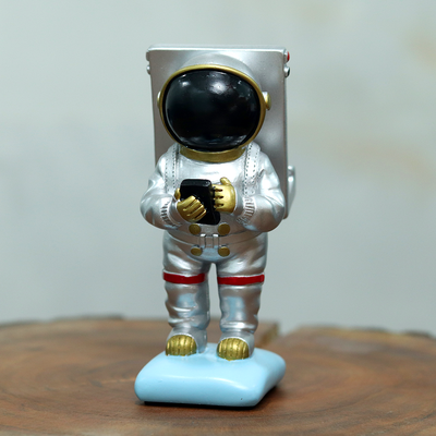 Astronaut mobile phone stand, silver in colour, which acts as great office/ desk decor.